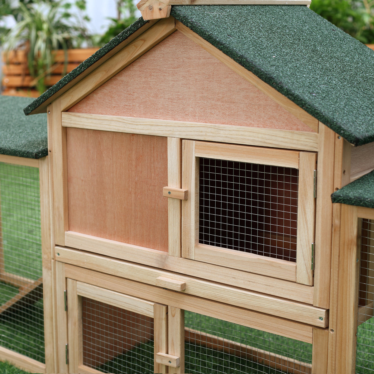 Close-up of the natural wood rabbit hutch's mesh window and green apex roof, garden behind