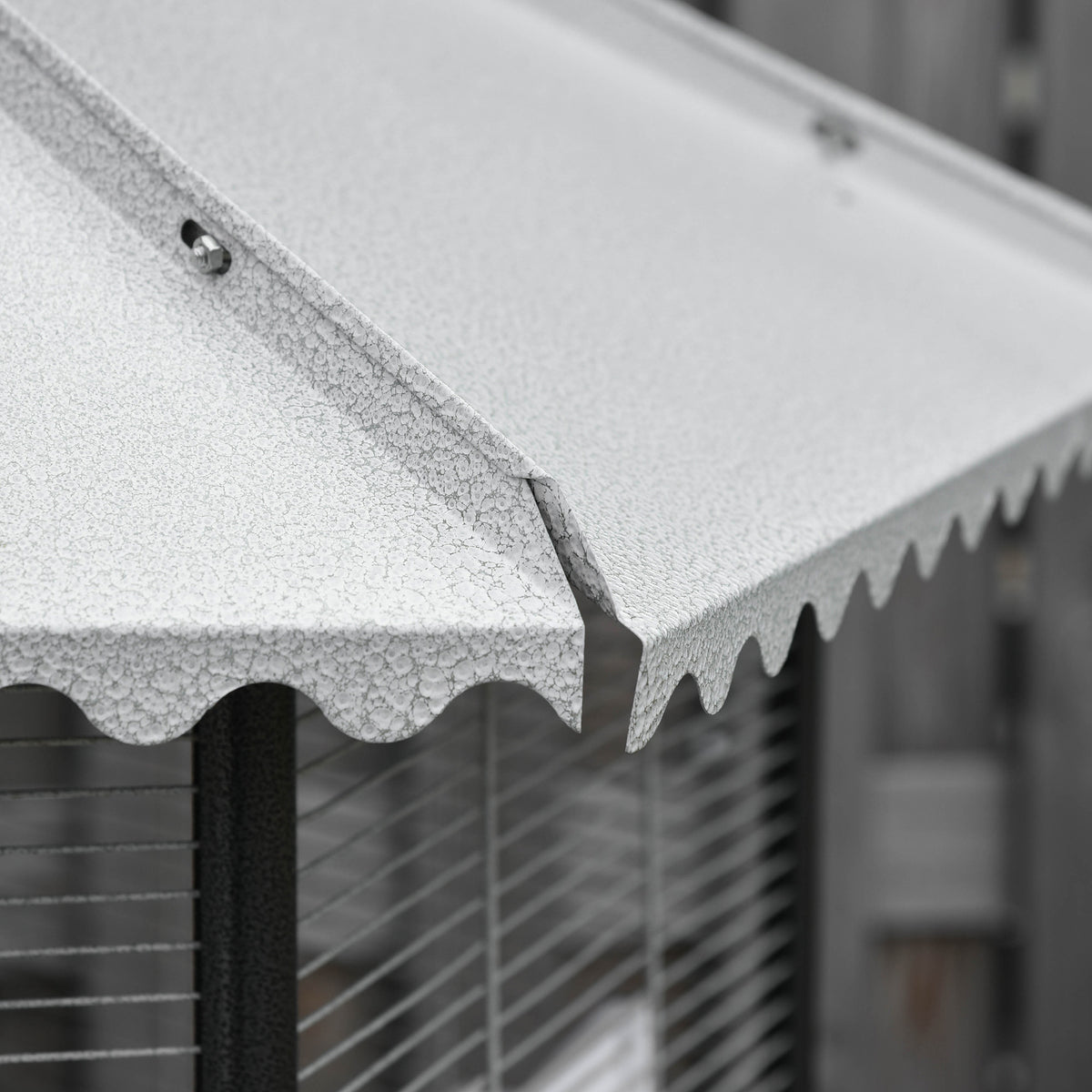 Close-up of the white aviary's scalloped canopy roof edge above its wire bars