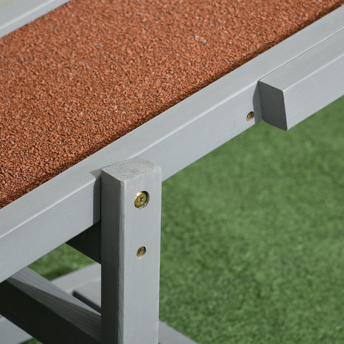 Close-up of the gray seesaw plank and its screwed wooden support frame over grass