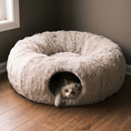 Beige plush cat tunnel bed on a wood floor with a cat looking out of the opening - wrenwood hero