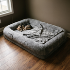 Giant grey plush human-size dog bed lounger on a bedroom floor with a small dog asleep on it - wrenwood hero