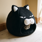 Black plush cat-face covered pet bed nest with a grey cat peeking out of the opening - wrenwood hero