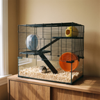 Dwarf hamster sits in the bedding of the glass-base wire cage on a wooden sideboard.