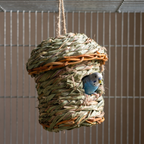 Hand-woven straw bird nest hut in a cage with a budgie at the entrance - wrenwood hero