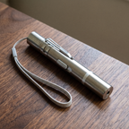 Silver handheld laser cat toy pointer with wrist lanyard on a wood table - wrenwood hero