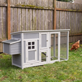 Brown hen stands on the lawn beside the grey wooden chicken coop and run.