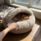 Hand resting on the plush rim of the hooded donut bed while a cat naps inside - wrenwood ugc lifestyle v2