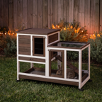 Brown elevated rabbit hutch at night with bunny inside, closed roof and warm string lights behind - wrenwood hero v2