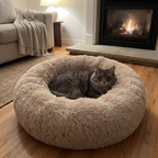 Grey cat curled in the calming donut cuddler bed by a lit fireplace on a winter evening